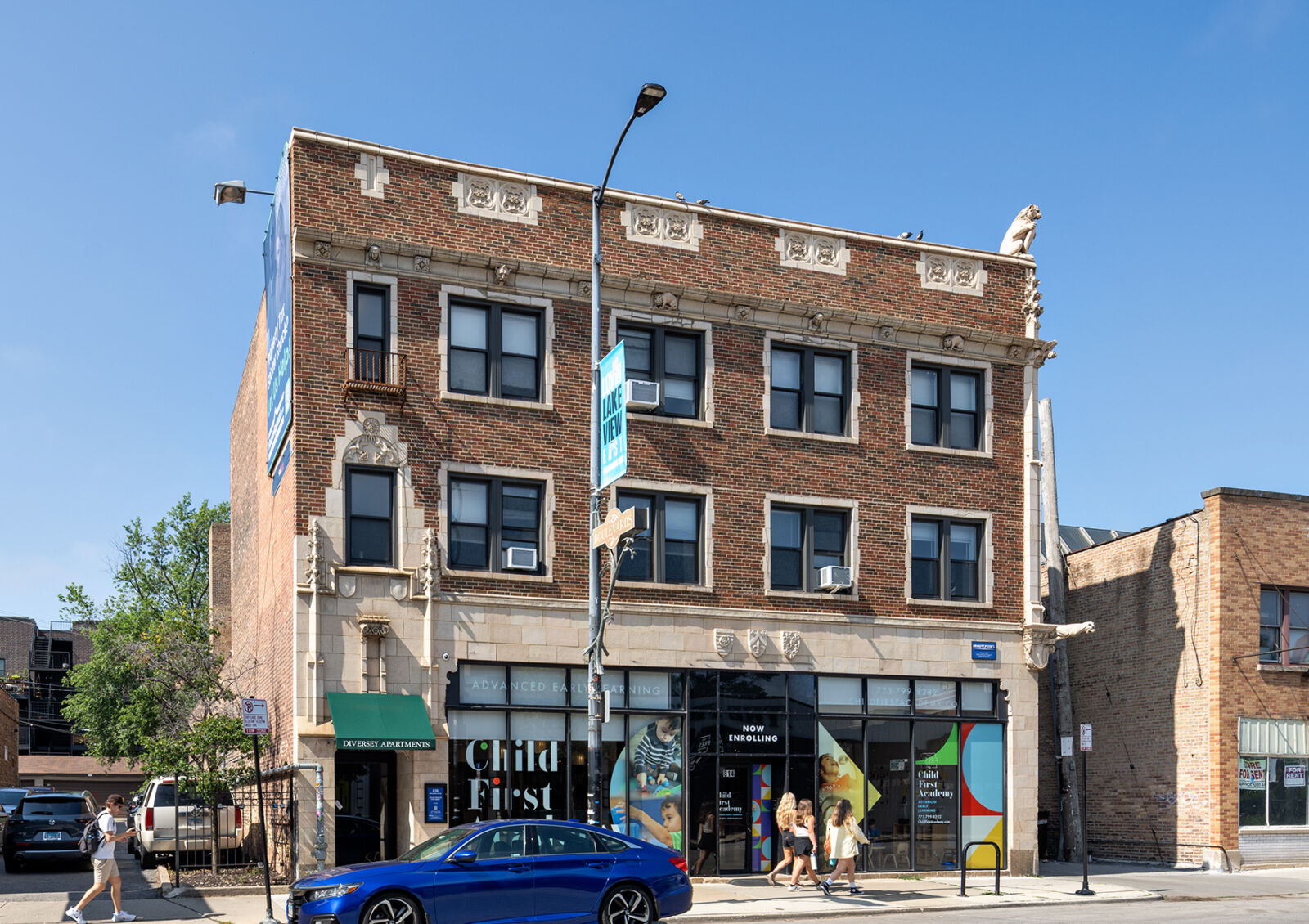 Three-story red brick apartment building with decorative stone accents and ground-floor storefron...