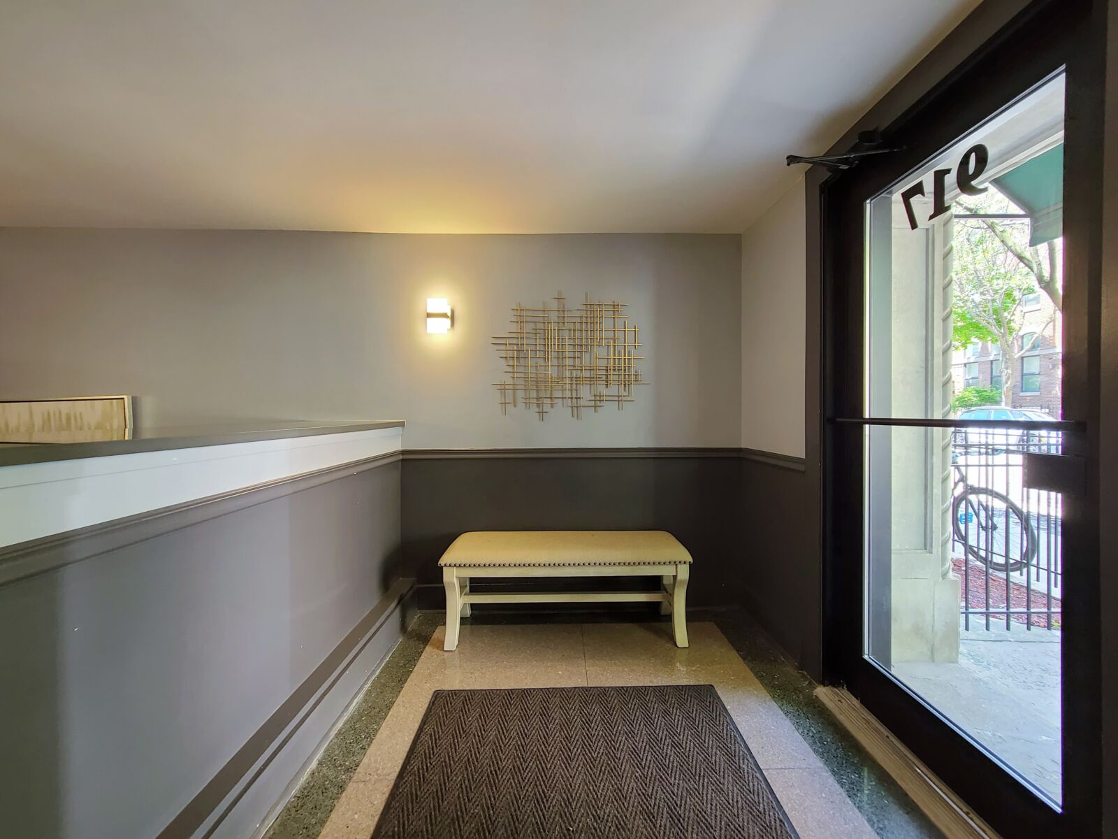 Lobby entry with glass door, cushioned bench seating, and wall-mounted gold sculpture accent.