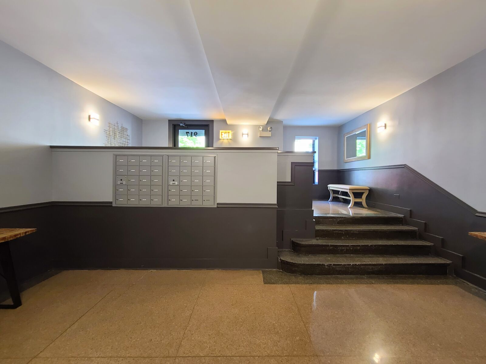 Apartment lobby with central mailboxes, tiered entry steps, and bench seating by a bright window.