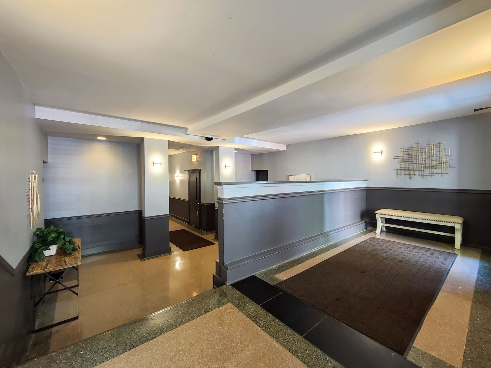 Spacious apartment lobby with soft lighting, entry bench, and decorative greenery on wood console.