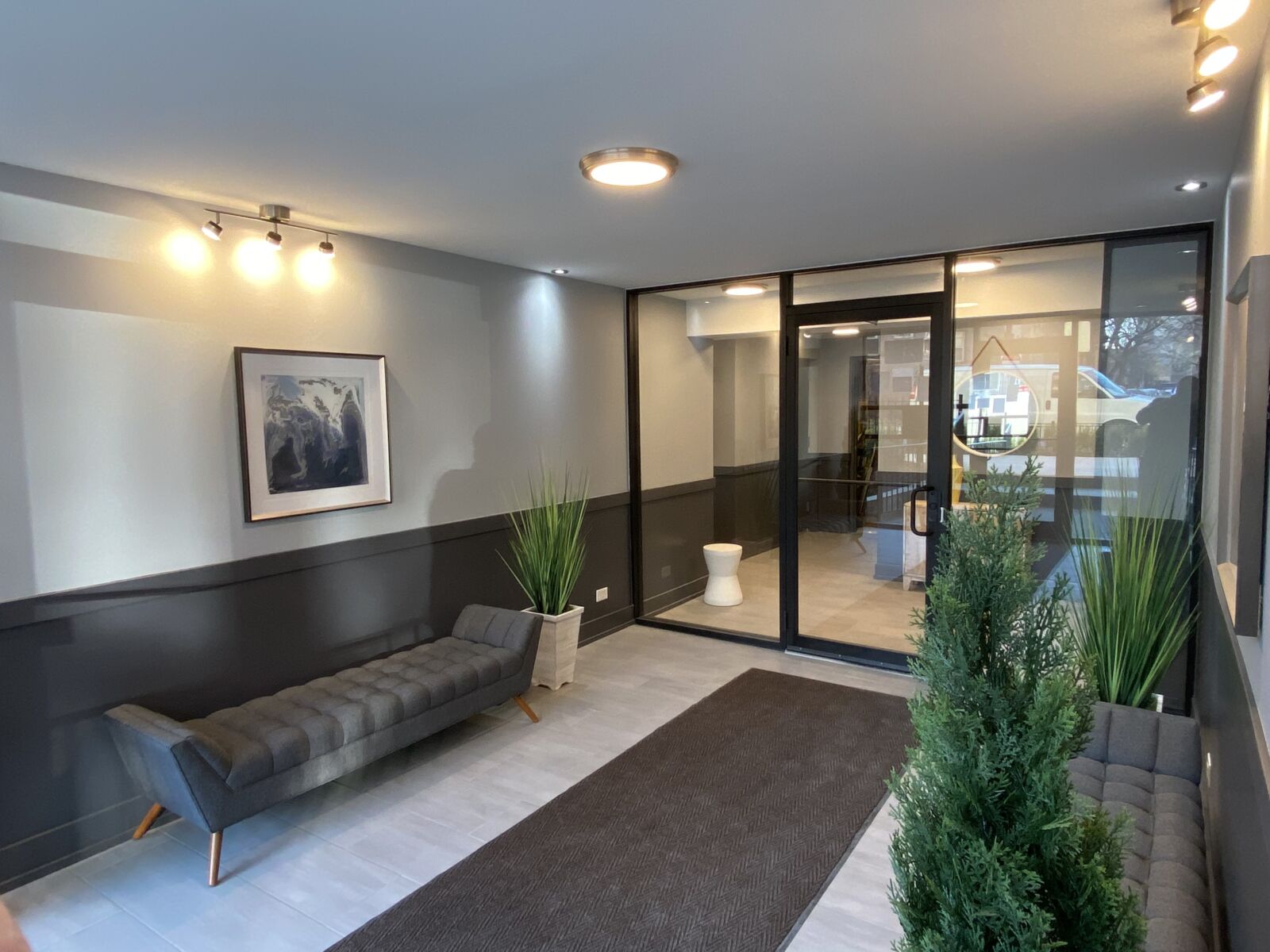 Lobby with modern gray seating, glass entryway, indoor greenery, and track lighting.