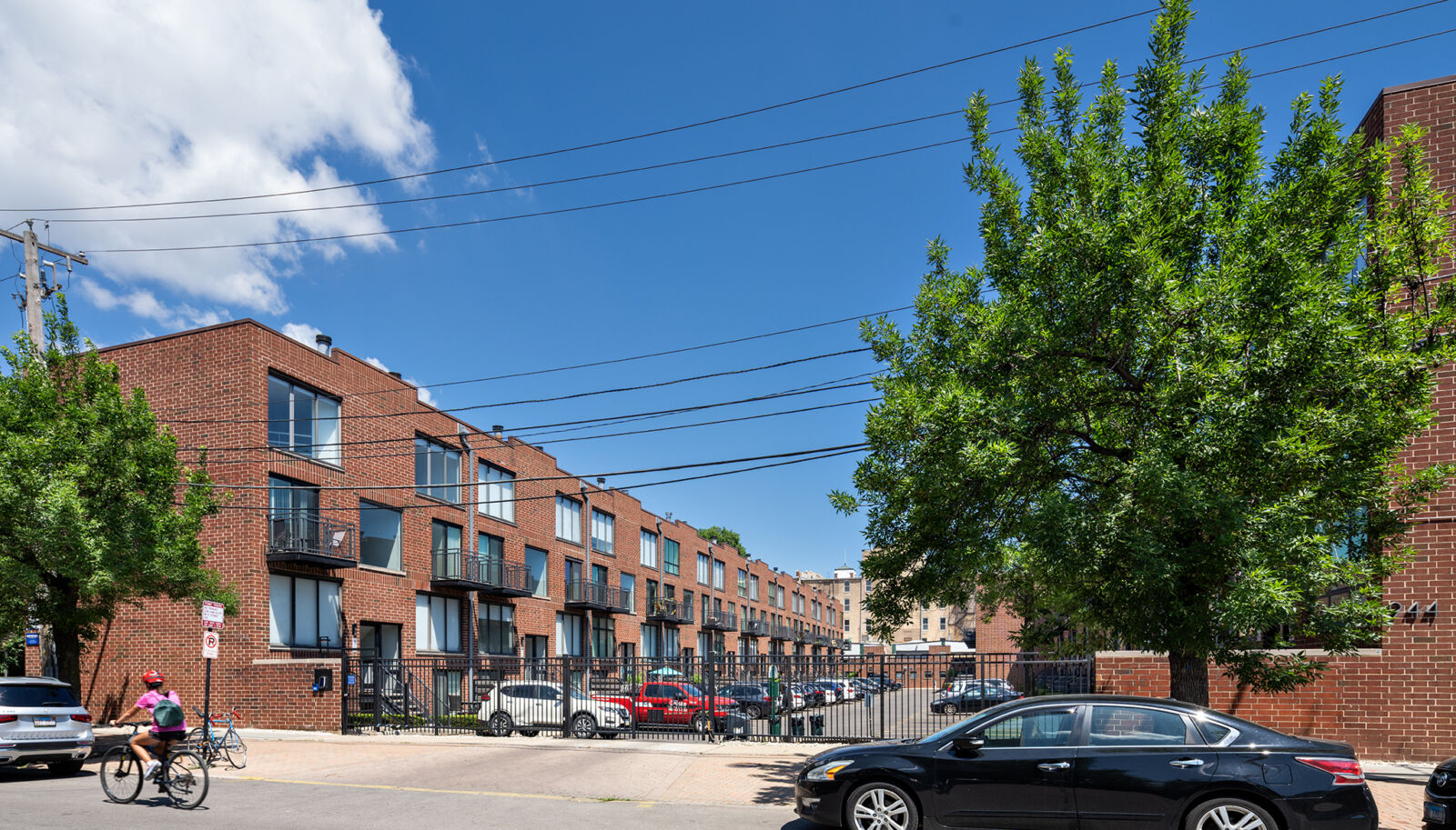 Contemporary red brick row of three-story townhome-style apartments with large windows and balcon...