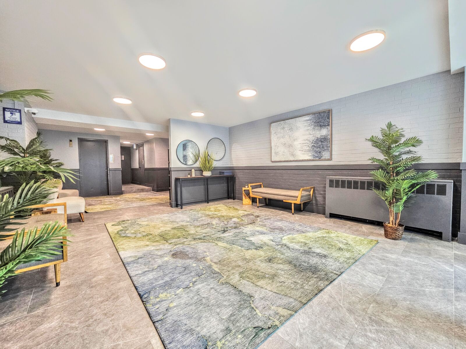 Lobby with contemporary benches, textured abstract rug, and tropical-style potted plants on gray ...