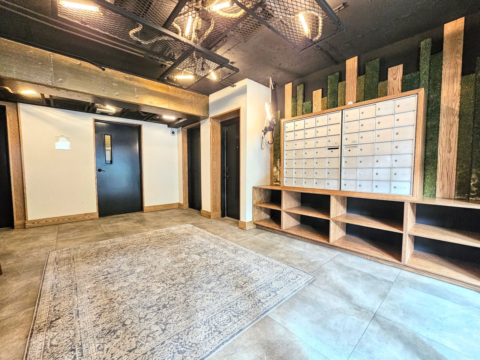 Lobby interior with wall-mounted mailbox units framed by vertical wood and green panels, open woo...