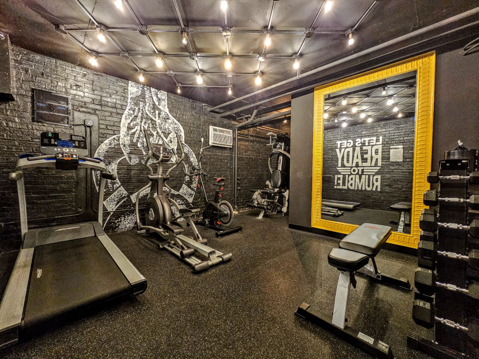 Alternate angle of the fitness room at 528 W Oakdale showing free weights, a workout bench, and a...