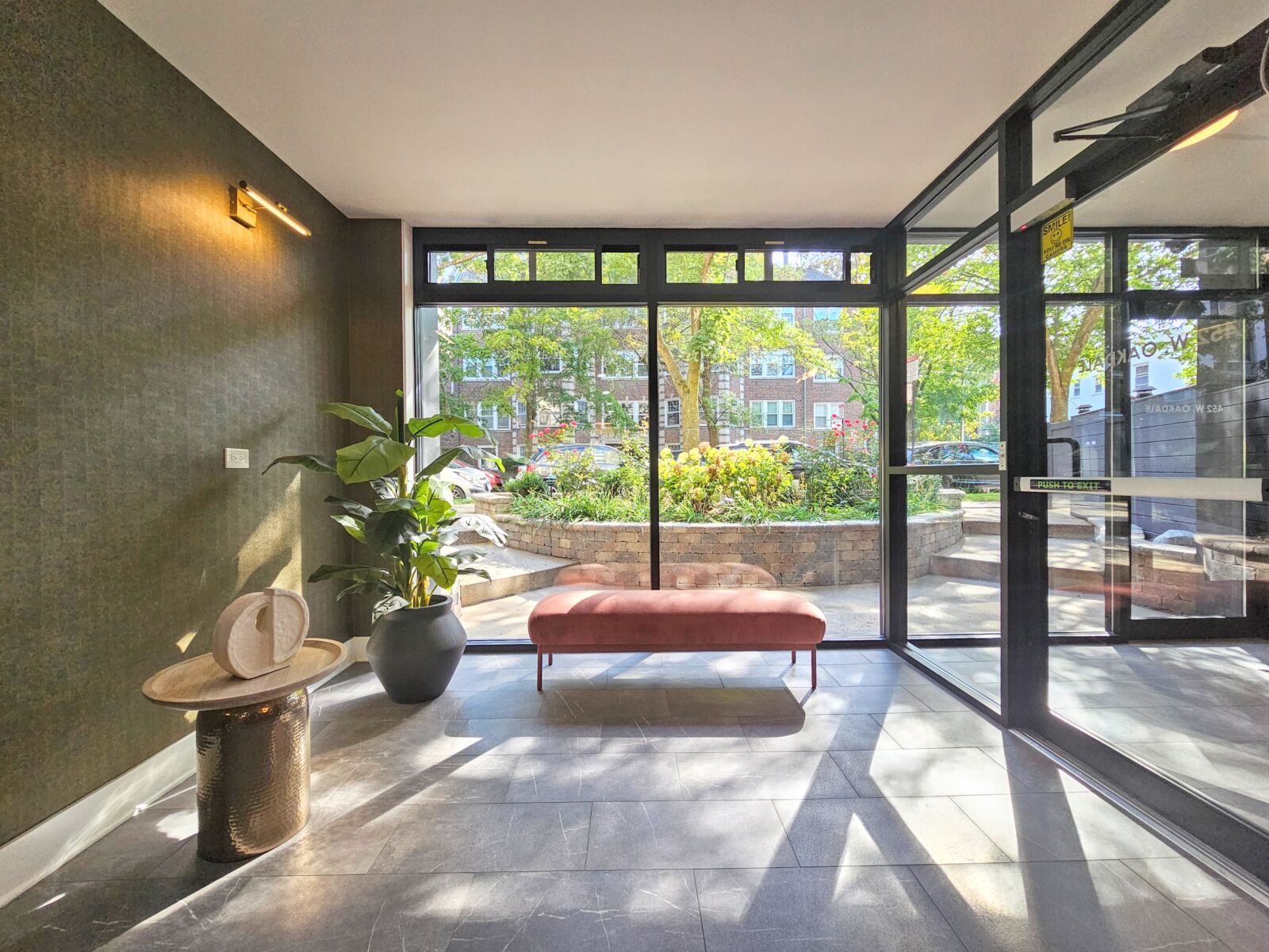 Lobby corner with bench seating, large windows, and potted plants overlooking landscaped entry.