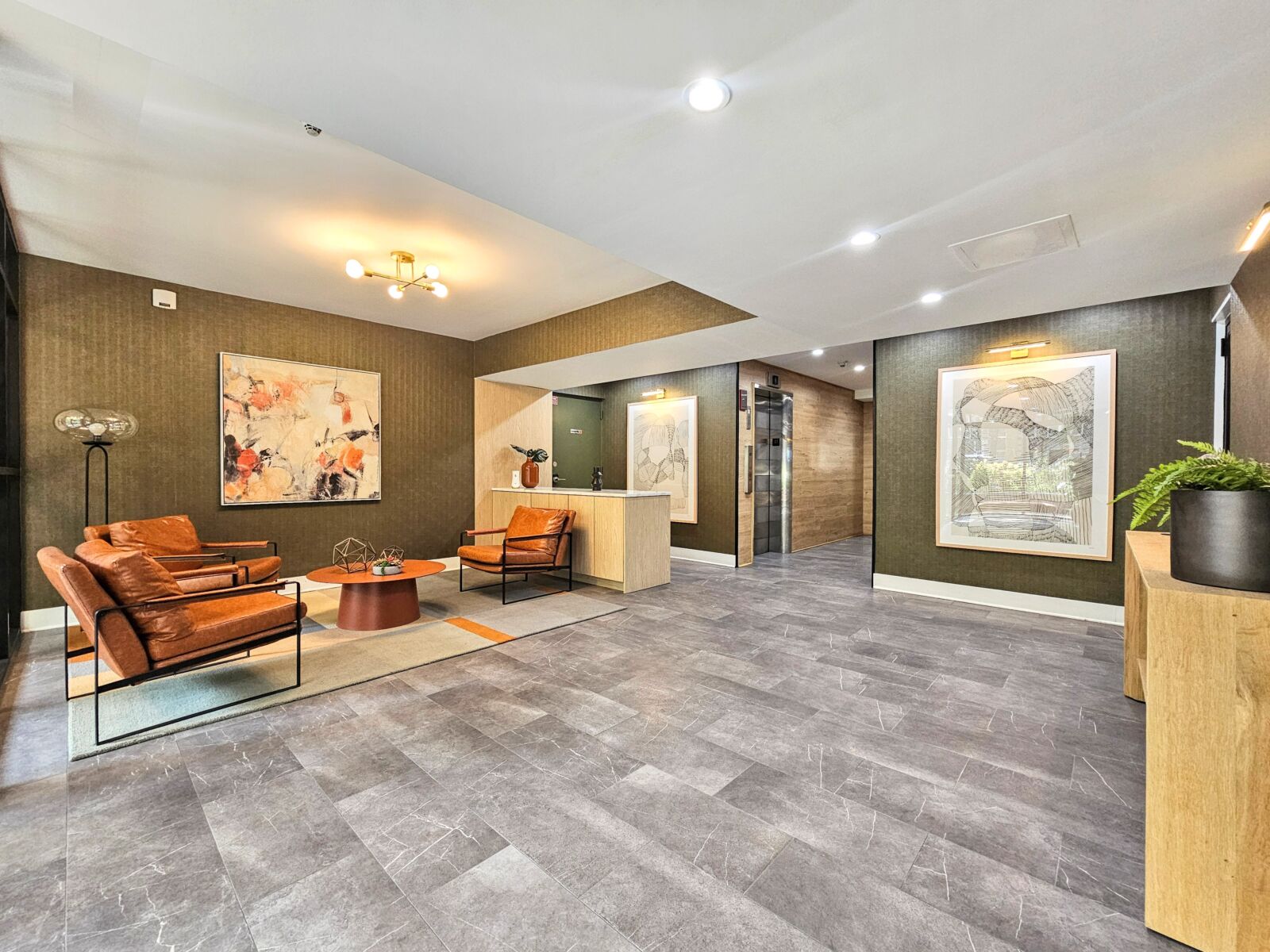 Lobby lounge with leather armchairs, abstract wall art, and neutral-toned tile flooring.