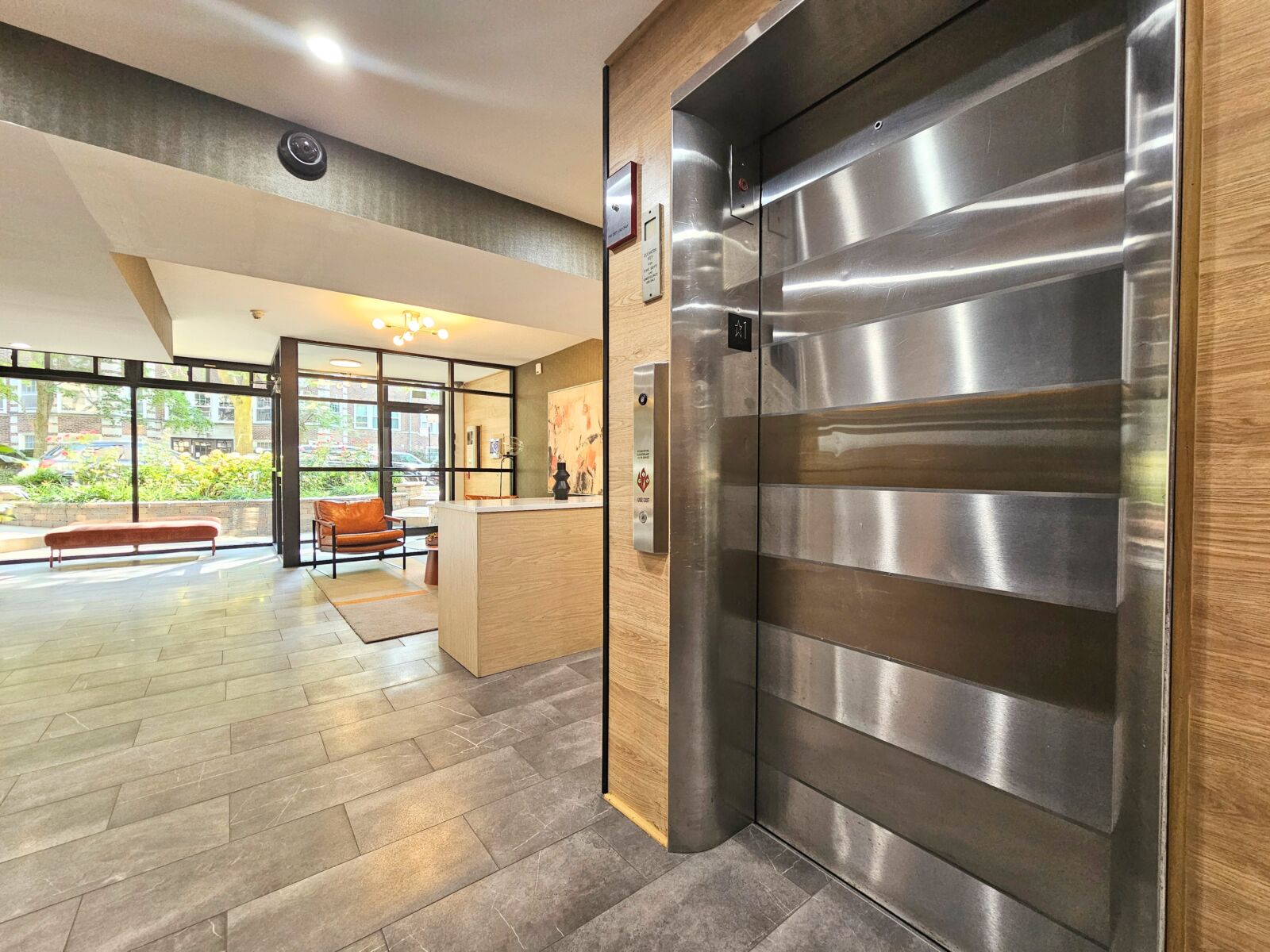 Lobby with stainless steel elevator, wood-accented reception desk, and floor-to-ceiling windows f...