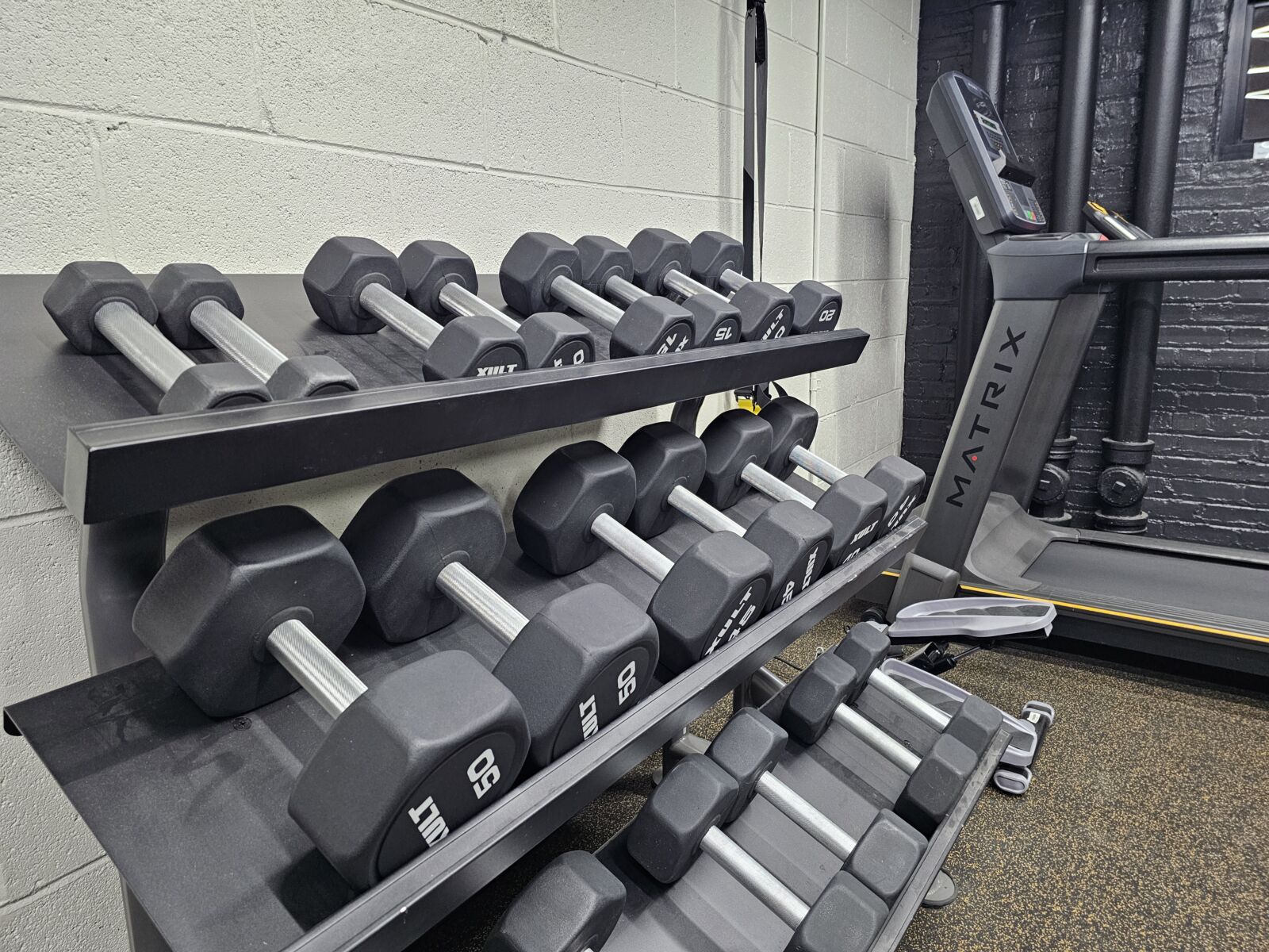 Fitness room with hex dumbbells on a rack and Matrix treadmill beside black accent wall.