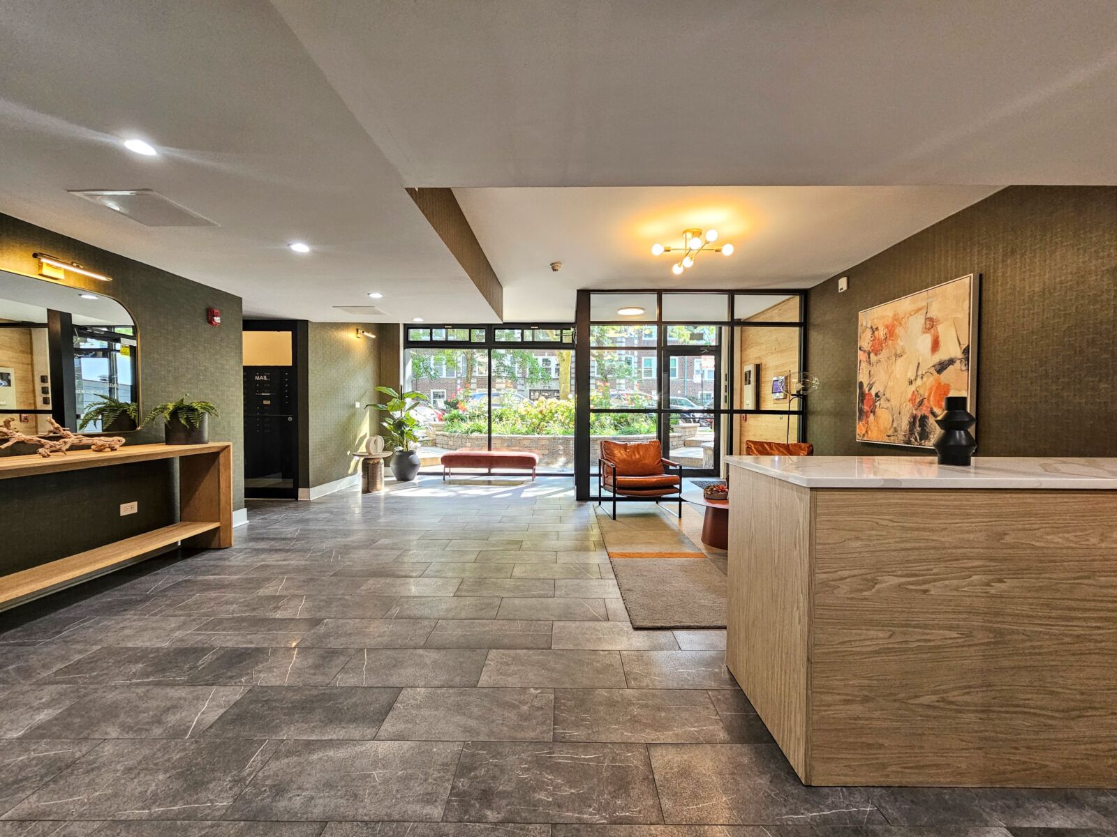 Lobby with floor-to-ceiling windows, slate tile floors, and warm-toned furnishings beside mail area.
