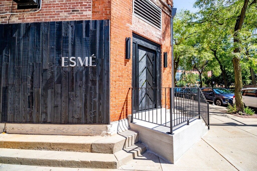 Exterior of red-brick corner building with black wood paneling and ramp entry labeled “ESMÉ.”