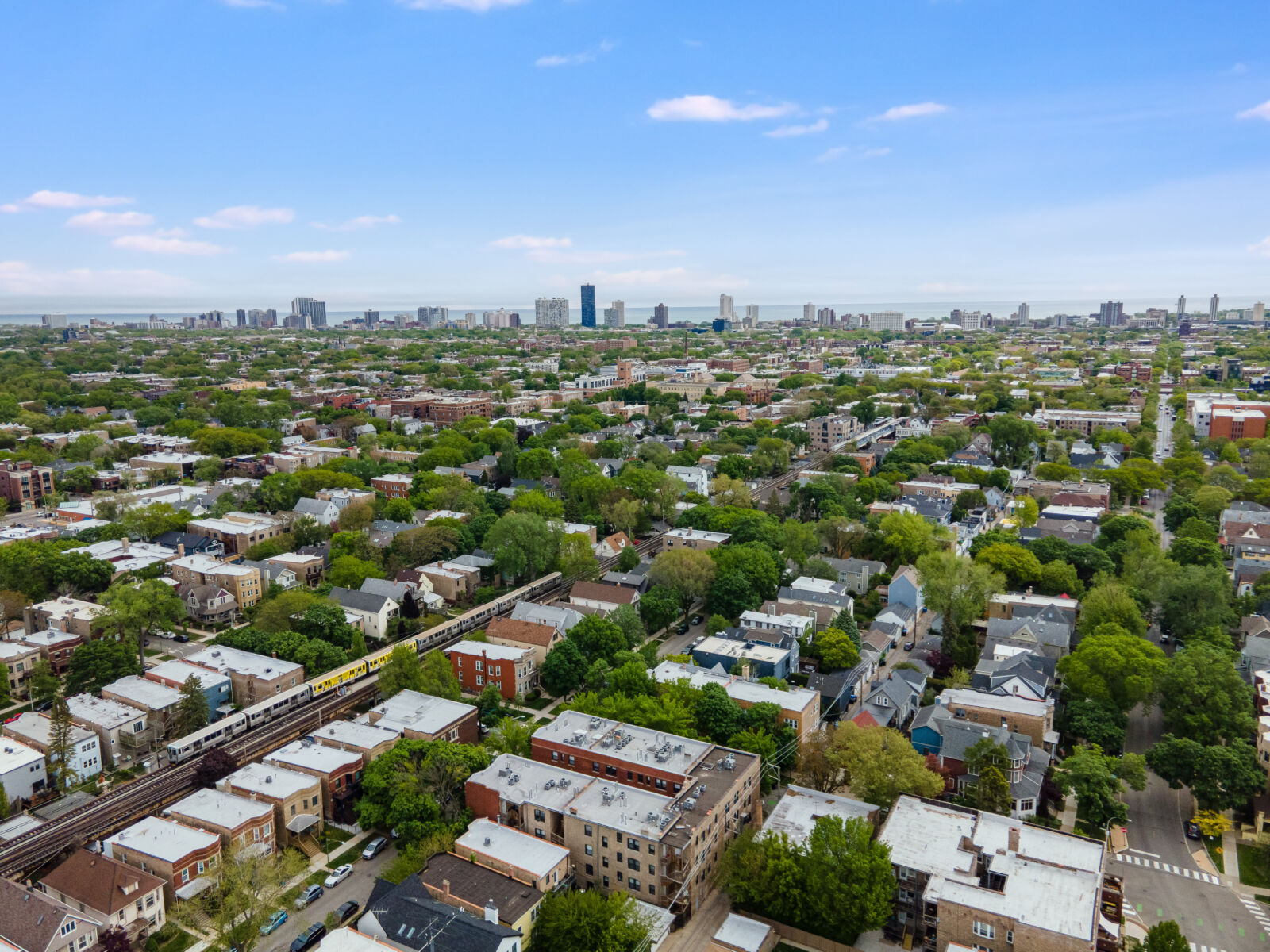 Aerial view of a tree-lined Chicago neighborhood with a CTA train passing through and Lake Michig...