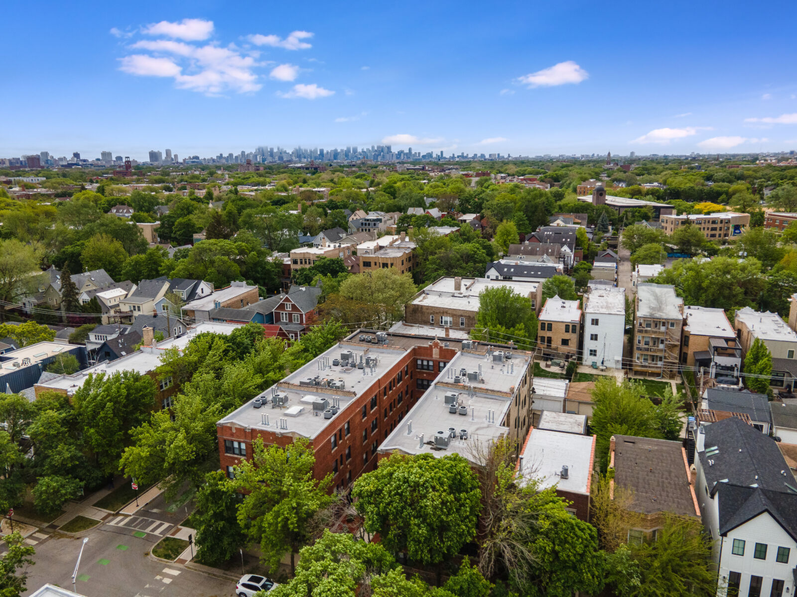 Aerial view of residential rooftops and trees in a Chicago neighborhood, with downtown skyline fa...