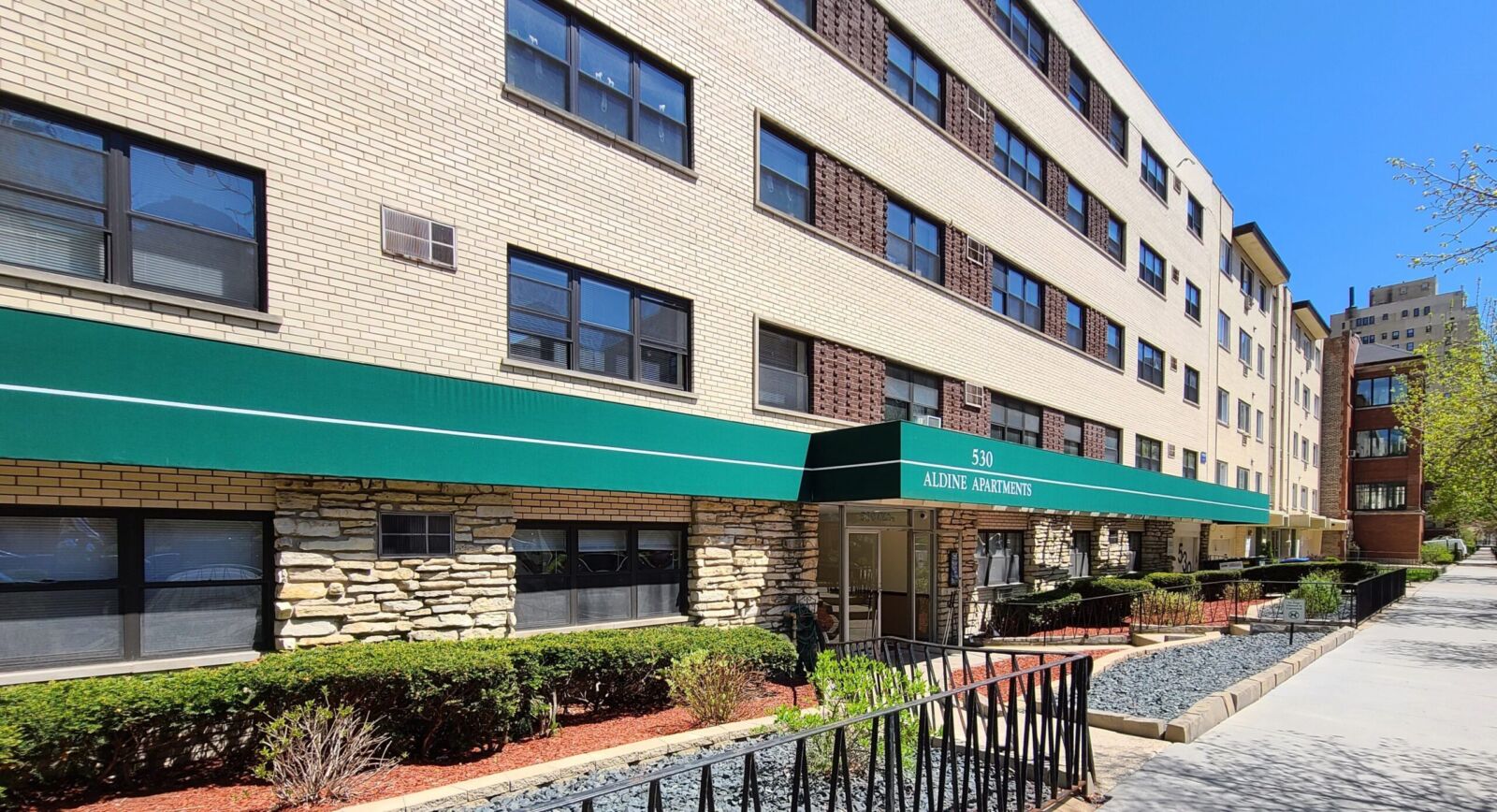 Mid-century style apartment building at 530 W Aldine Avenue with light brick exterior, green awni...