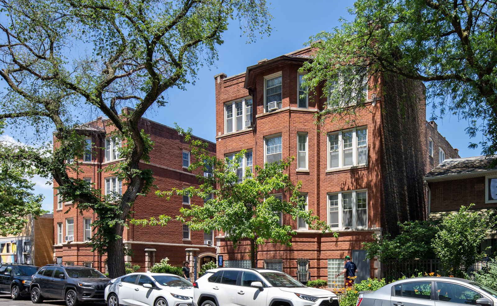 Red brick corner apartment building with bay windows and leafy street trees at 550–560 W Aldine A...