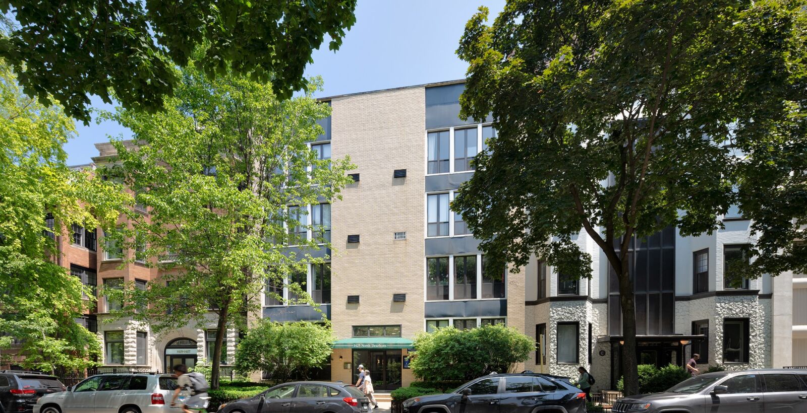 Modern beige brick apartment building with dark window panels and green awning at 1425 N Dearborn...