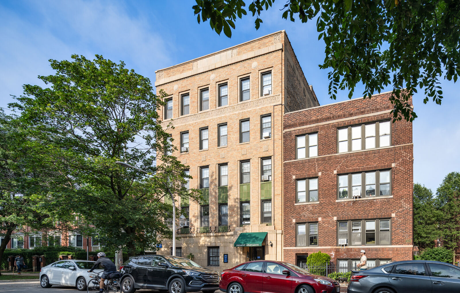 Five-story tan brick apartment building with decorative stone trim and green glazed terra cotta p...