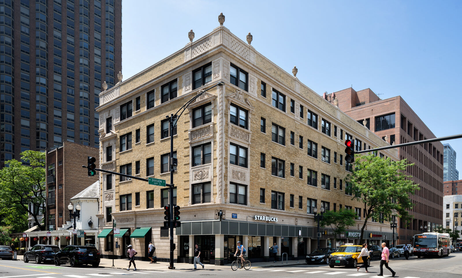 Historic tan brick apartment building with ornate terra cotta detailing and retail storefronts, i...