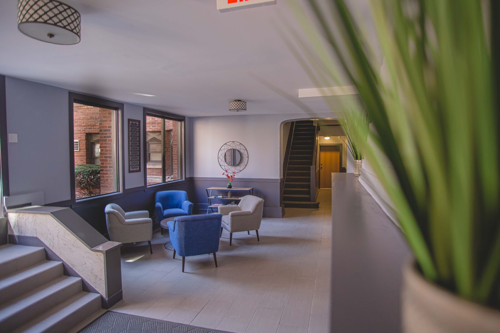 Lobby with modern seating, large windows facing brick courtyard, and accent lighting over stair a...