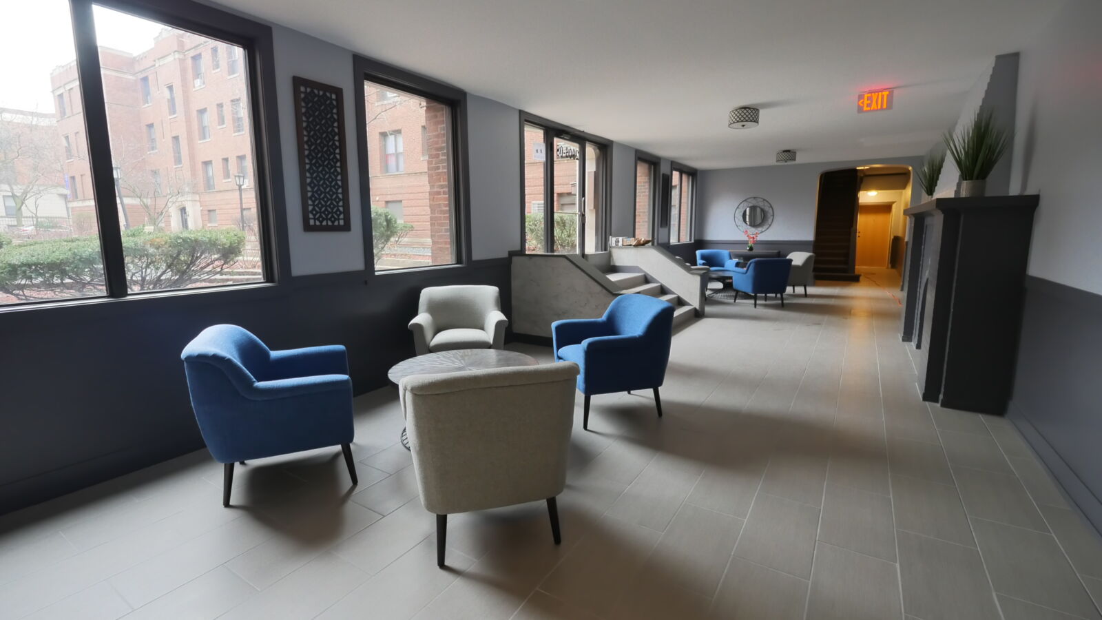 Lobby with full-height windows, blue and gray lounge chairs, and tiled floors overlooking courtya...