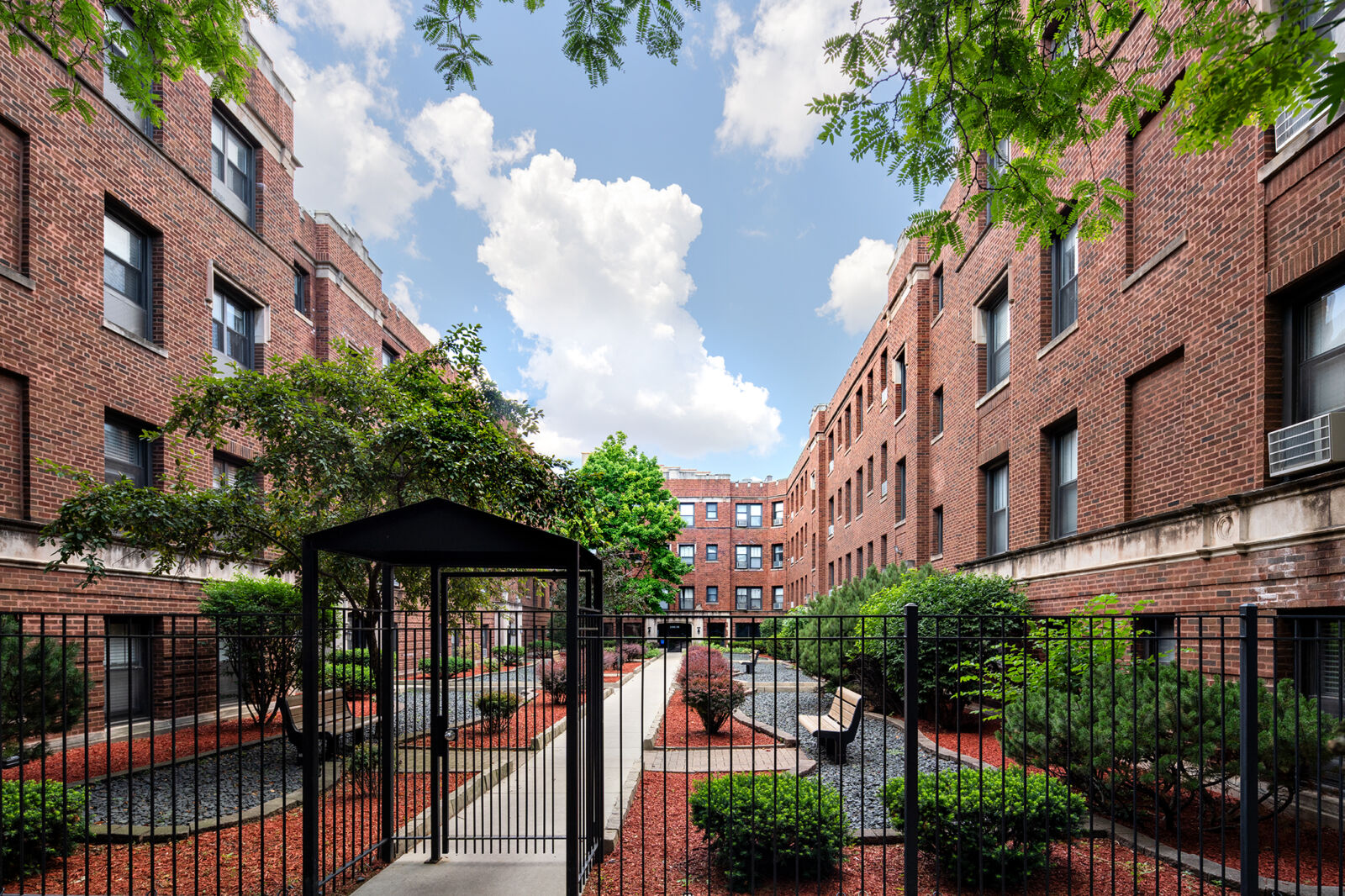 View through a black metal gate into the landscaped courtyard of 2900–2914 North Mildred in Chica...