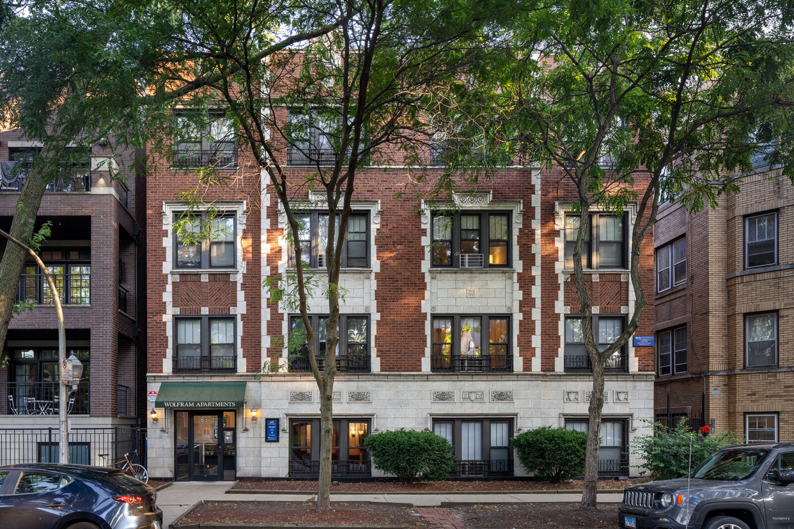 A classic three-story red brick apartment building with detailed limestone trim and a green awnin...