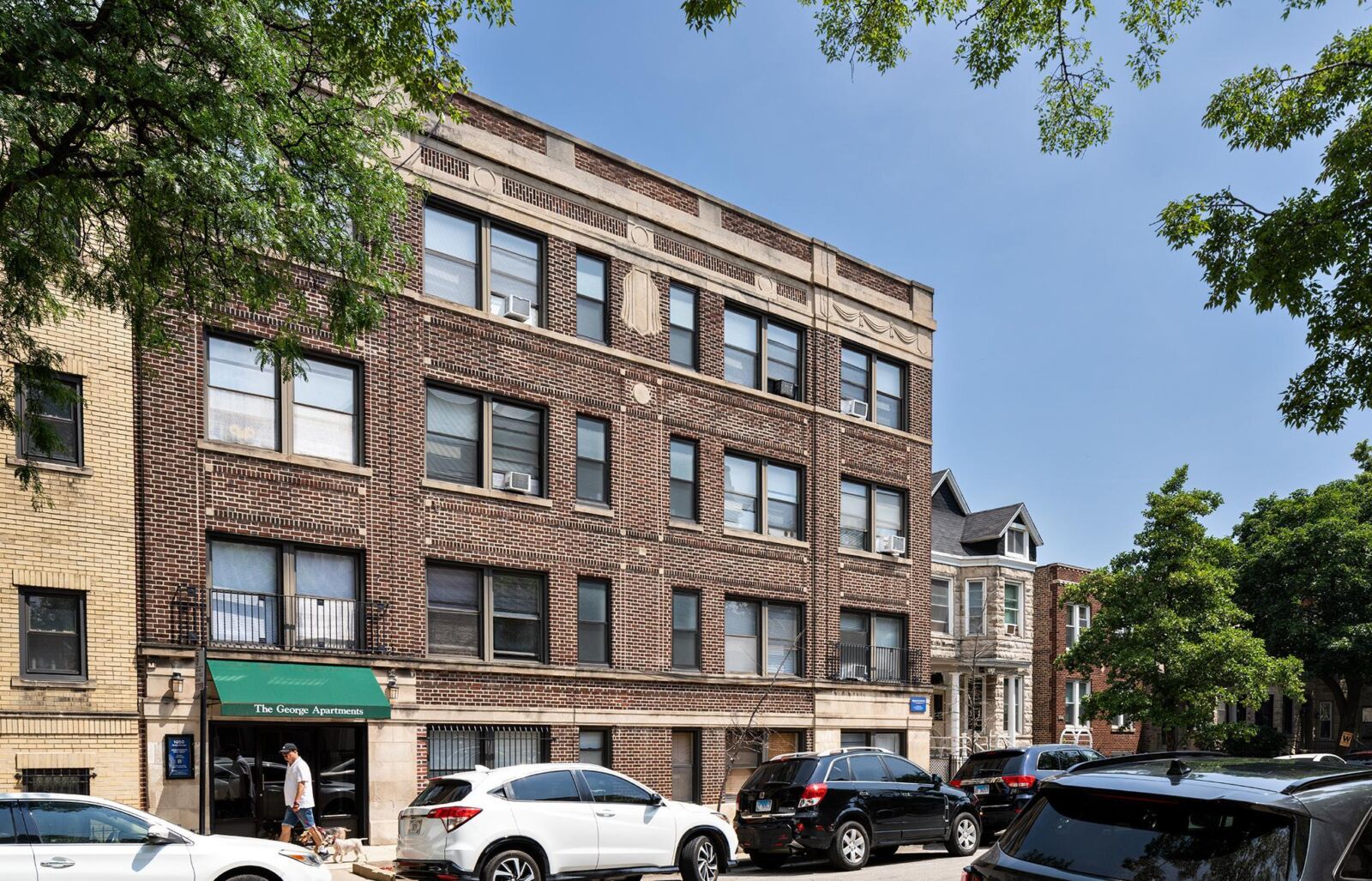 Four-story red brick apartment building with decorative stone trim and a green awning labeled ‘Th...