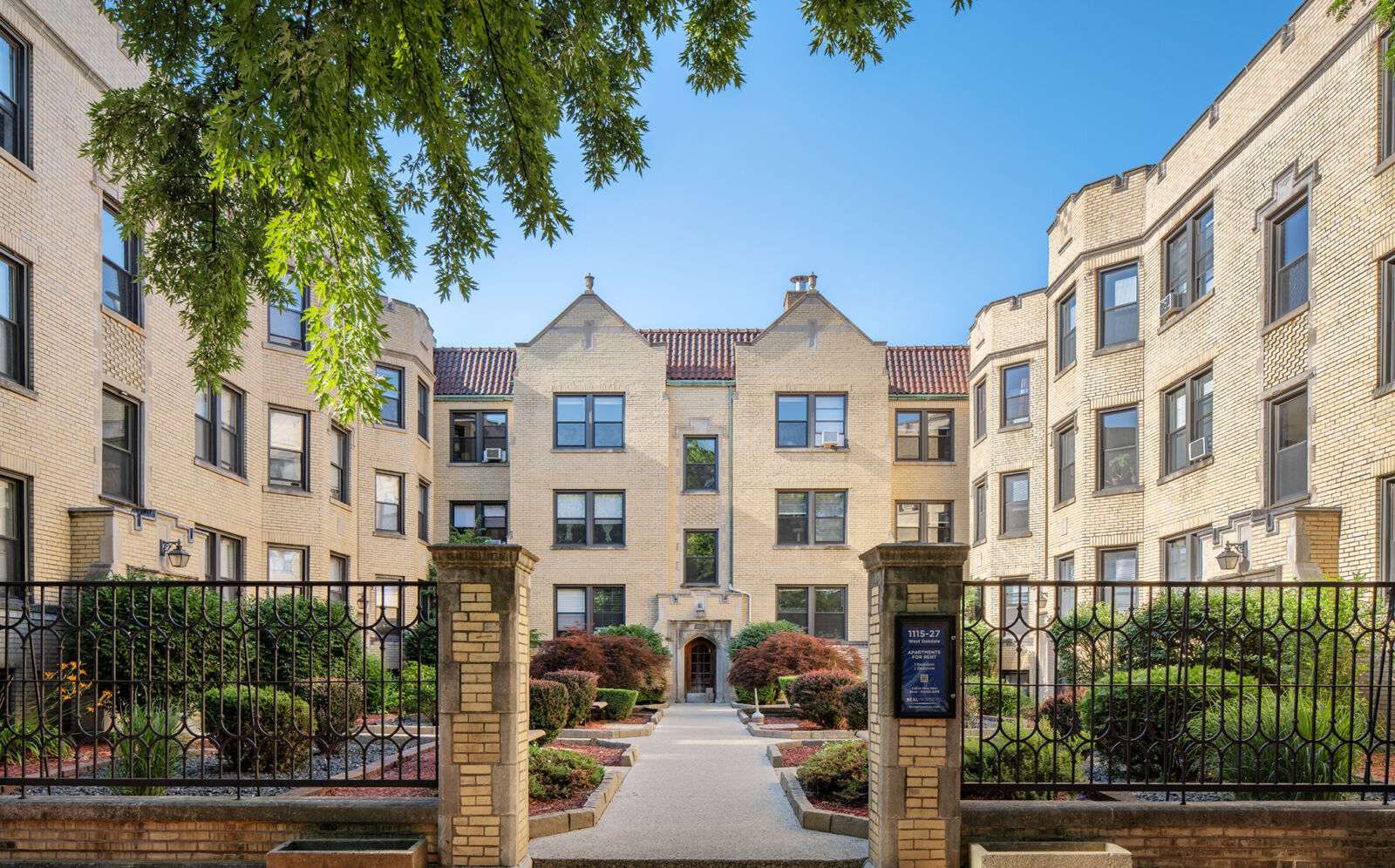 Three-story yellow brick apartment building with a gated courtyard and central entrance at 1115–1...
